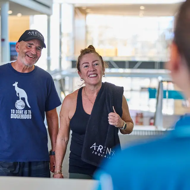 Two gym members being greeted at Gym reception by an Arena Joondalup staff member