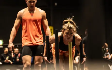 Female team member pushing a sled and male team member supporting at HYROX event