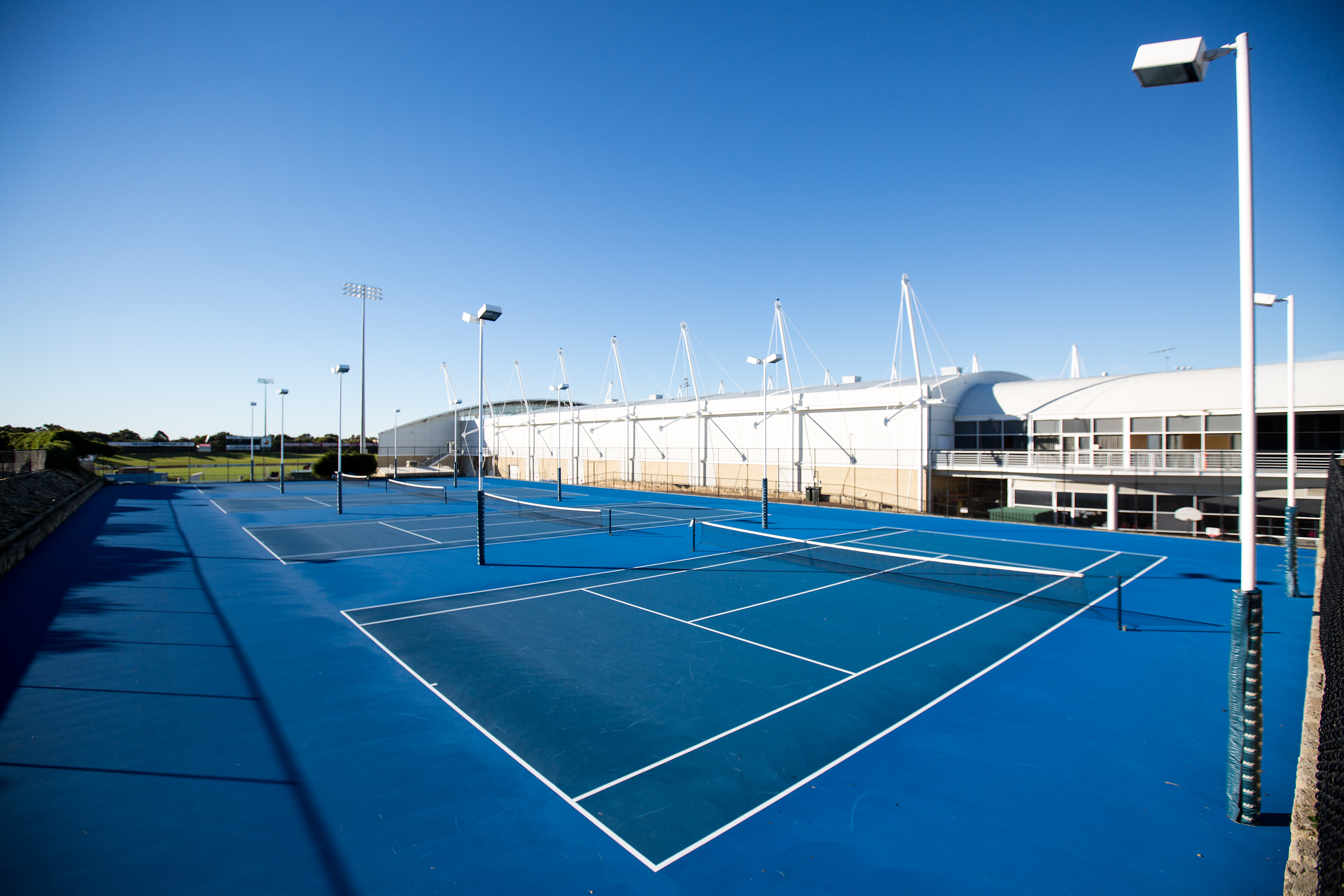 A photo of three side by side blue tennis courts at Arena Joondalup