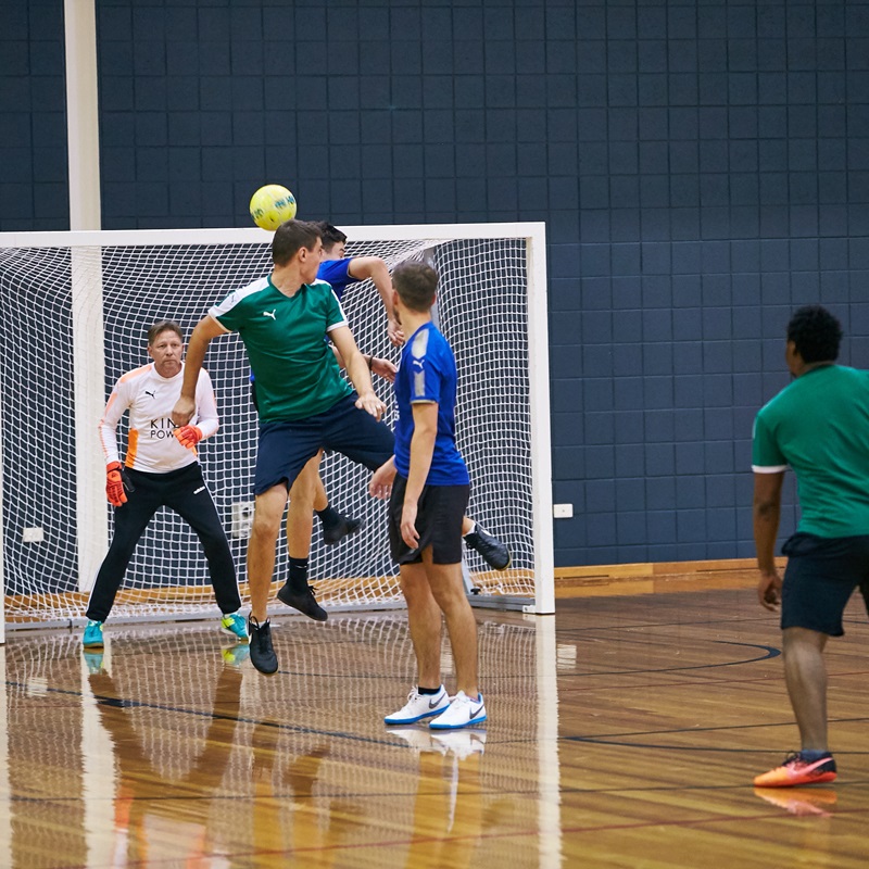 Two players contesting the ball near the goals in a men's futsal game