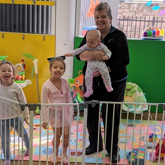 Crèche attendant holding a baby next to two happy preschoolers
